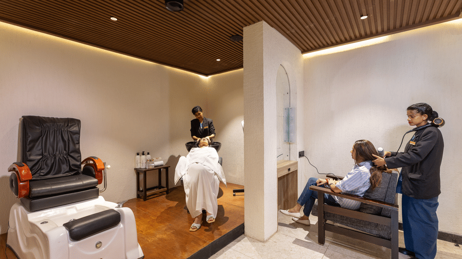 An indoor seating area with armchairs, a person seated, and another person standing nearby holding equipment.