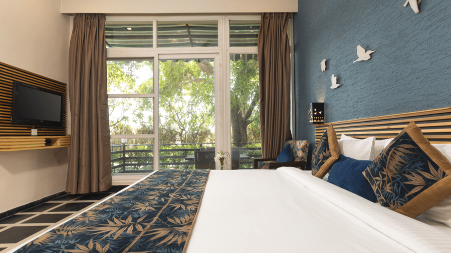 Nature View Suites view showing a bed with a dark runner, a TV stand, and a window with curtains at The Golden Tusk, Jim Corbett