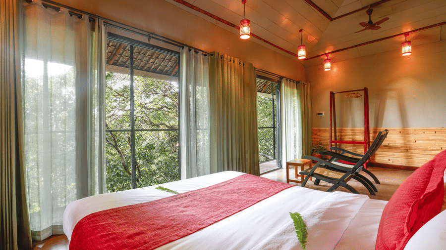 A bed placed in a room with tall glass windows and ambient lighting | Vythiri Resort, Wayanad