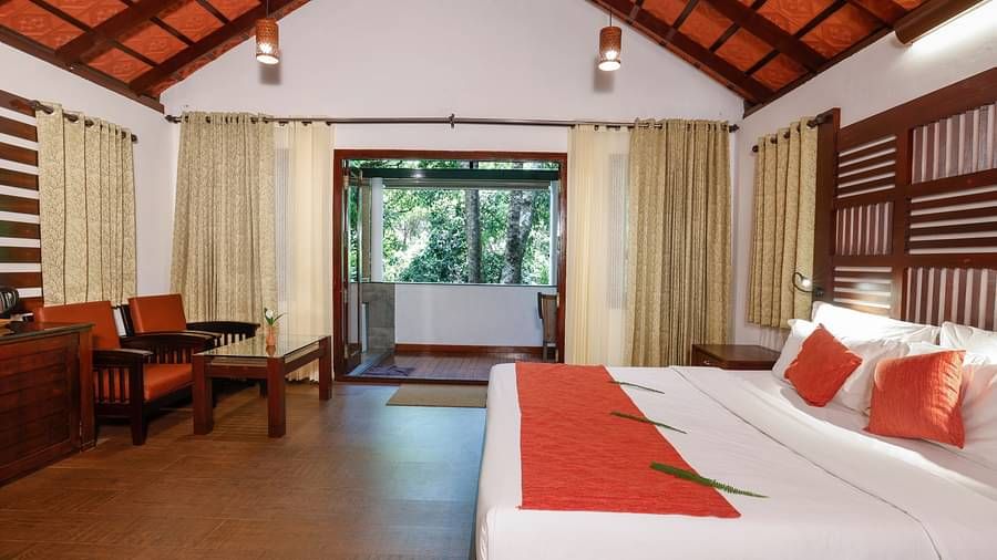 A side view of a room that has a bed, two chairs, and a balcony with forest views | Vythiri Resort, Wayanad