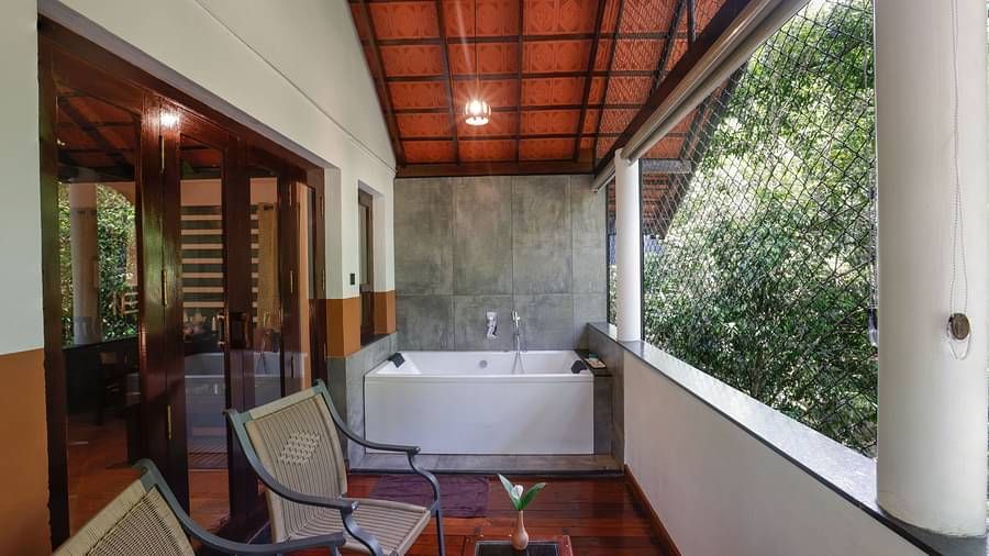 Two chairs, a table, and a Jacuzzi in the balcony that has forest views | Vythiri Resort, Wayanad