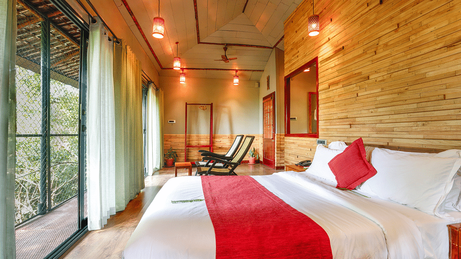 A bed in a room with tall glass windows and ambient lighting | Vythiri Resort. Wayanad