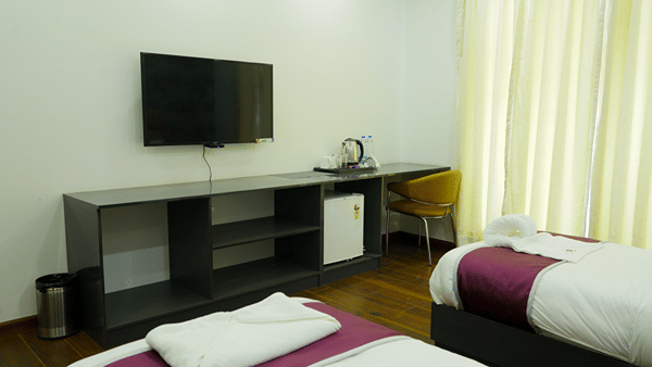 Bedroom of Lime Tree Hotel, Pulkit featuring a wall mounted television, a console, and maroon bedding.