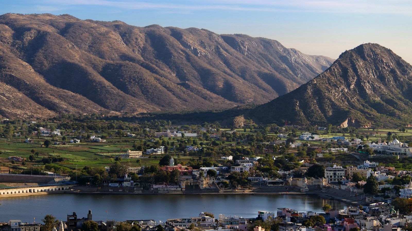 A serene landscape with a lake reflecting the sky, nestled amidst rolling hills.