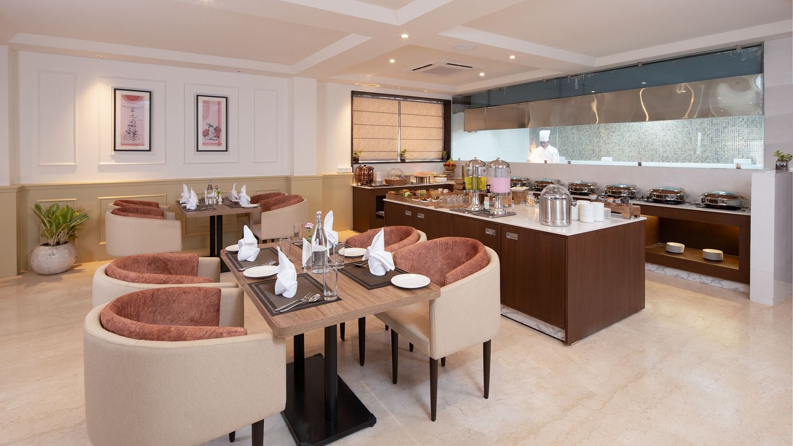 An image of a dining space with sofa chairs, centre table with hand towels and cutlery, and a buffet served at one corner - Brij Eternity, Vrindavan