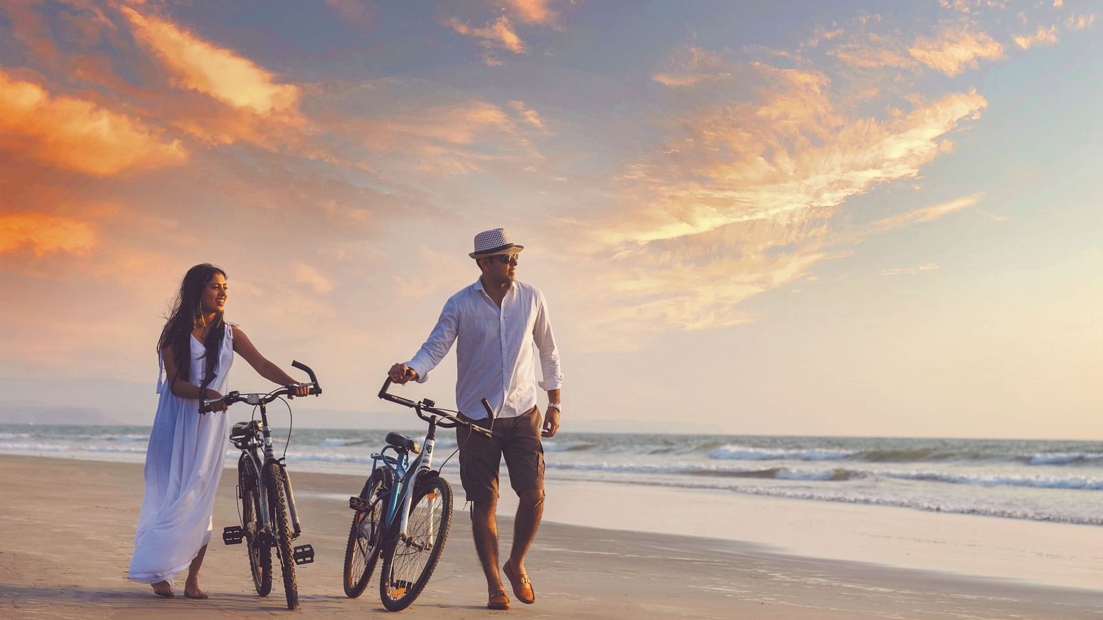 a couple walking on the beach while holding their cycles - Caravela Beach Resort Goa.