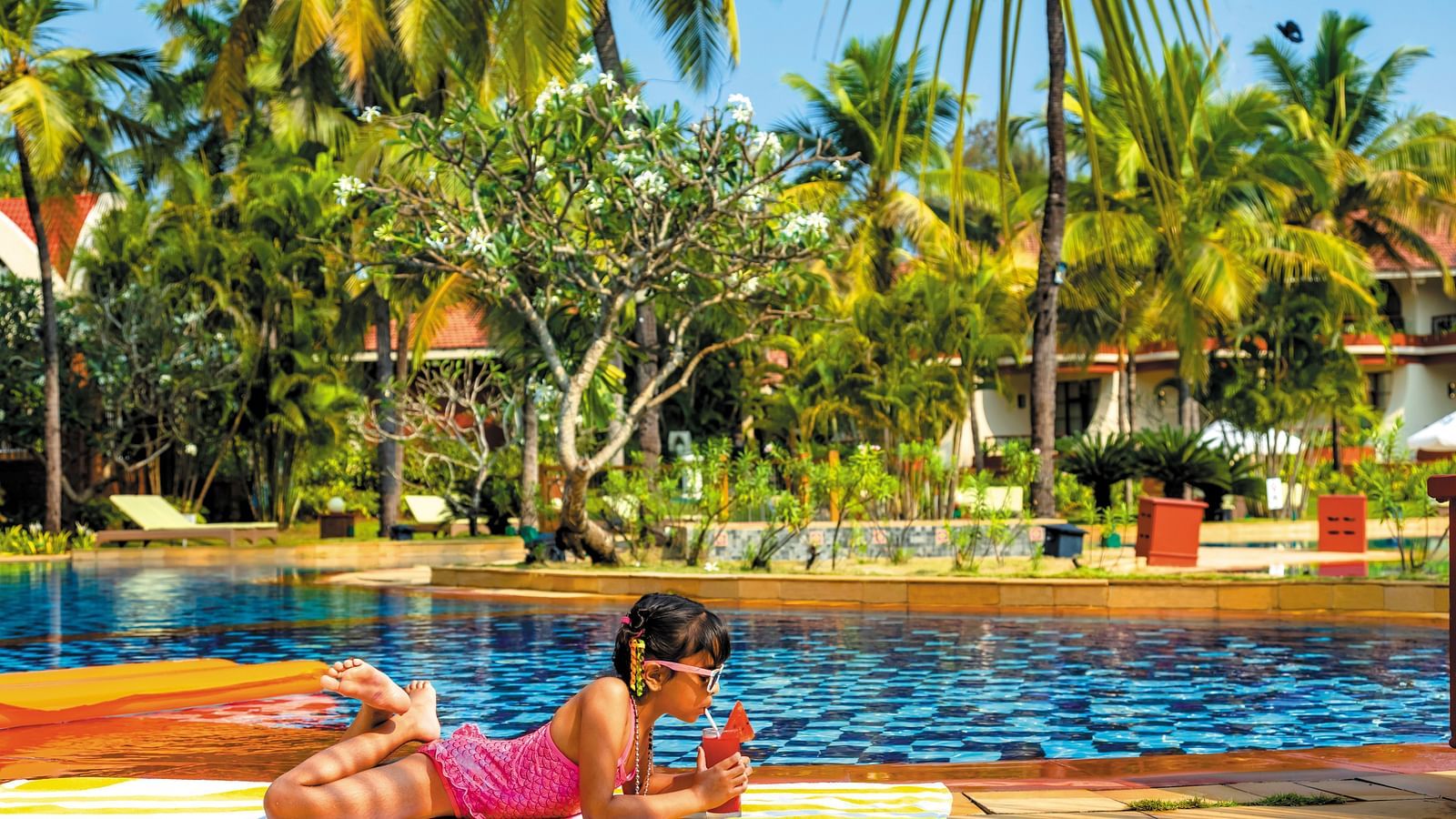 a woman lying down next to the swimming pool - Caravela Beach Resort Goa