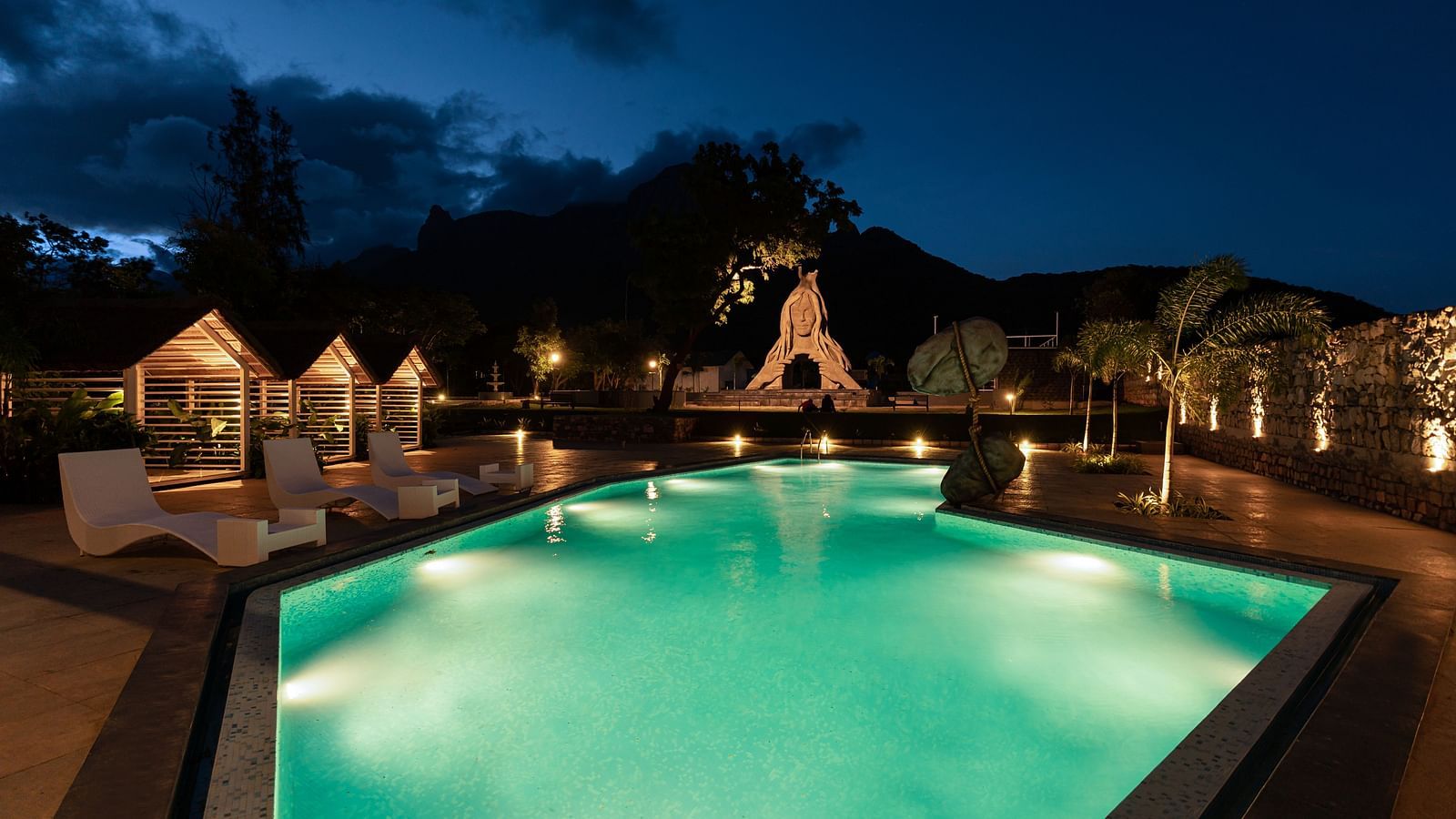 image featuring the expansive swimming pool in the night with a stone statue in the background - Darza Resorts