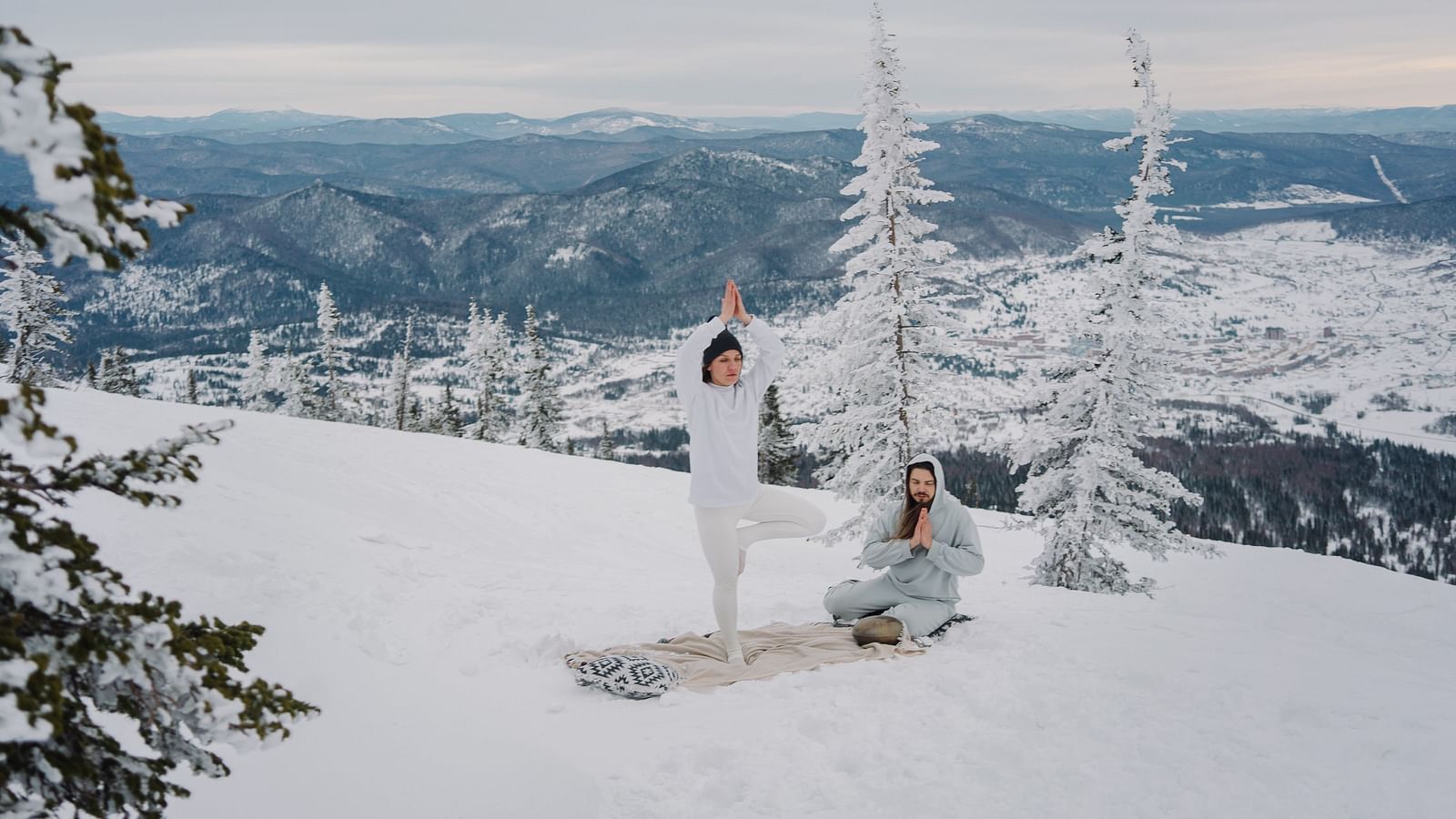 a couple performing yoga asanas together on a snow covered mountain