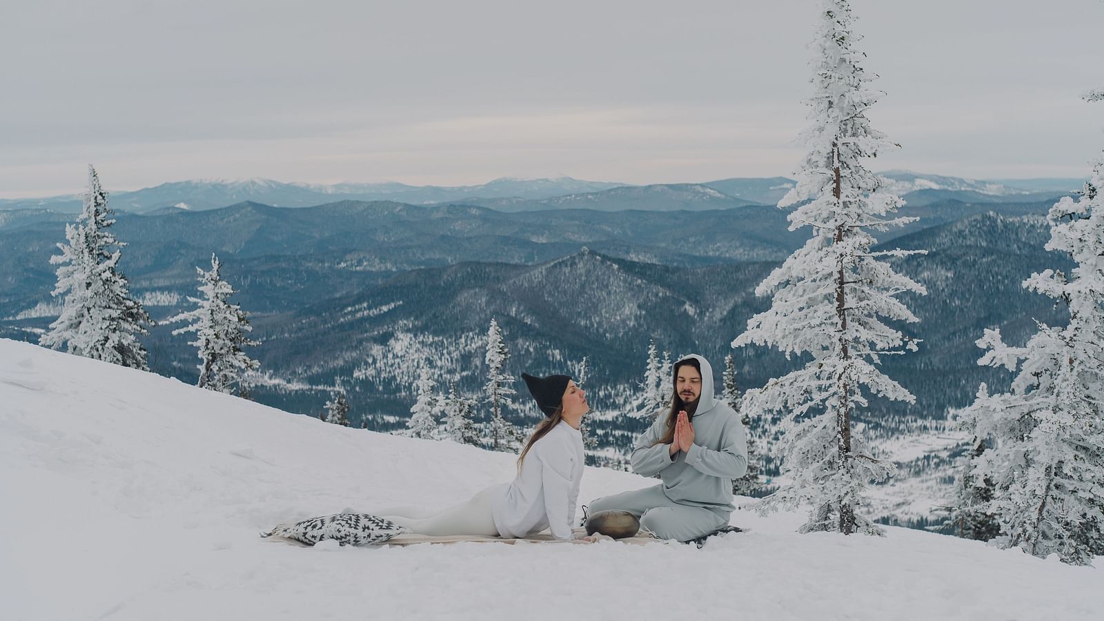 a couple performing yoga asanas together on a snow covered mountain