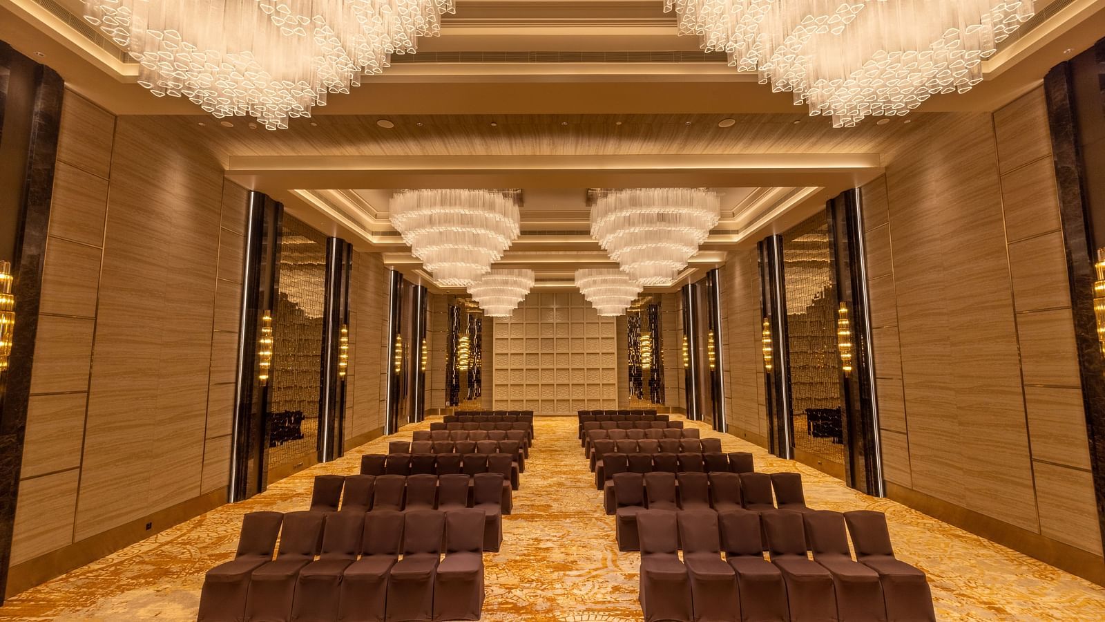 Luxurious banquet hall with rows of chairs and opulent hanging chandeliers - Grand Madurai by GRT Hotels