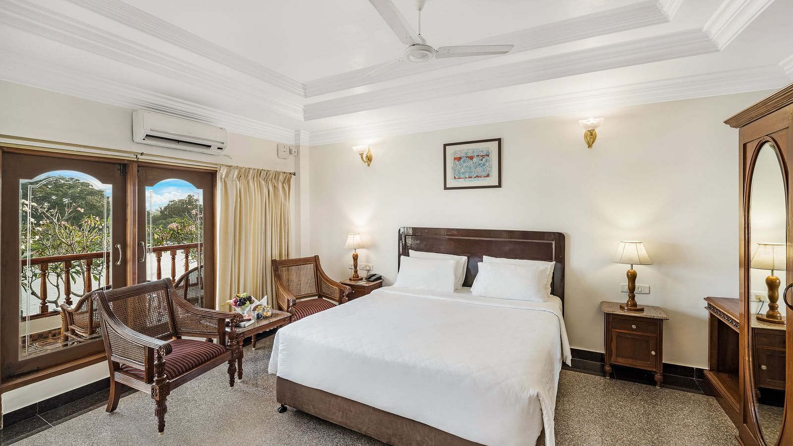 An image of the River Edge Heritage Room featuring a queen size bed, bed side table, lamps, and chairs - GReaT Trails River View Resort Thanjavur By GRT Hotels