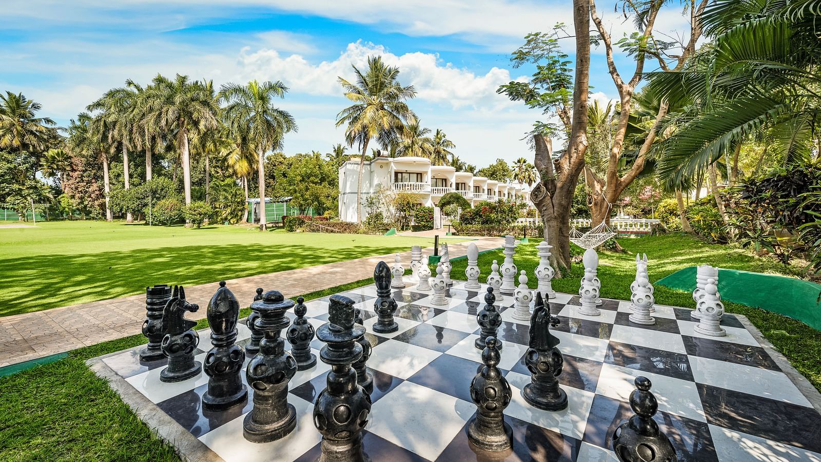 An image of a play area with a humongous chess laid on the lawn surrounded by lush greenery - GReaT Trails River View Resort Thanjavur By GRT Hotels