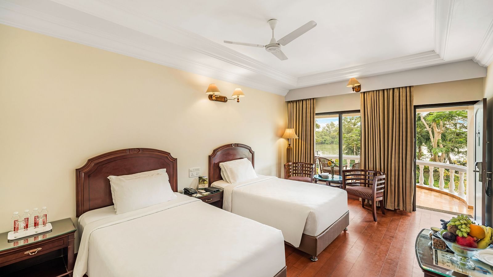 An image of the River View Room With Verandah featuring two single beds, bed side table, lamps, flat screen TV, and chairs - GReaT Trails River View Resort Thanjavur By GRT Hotels