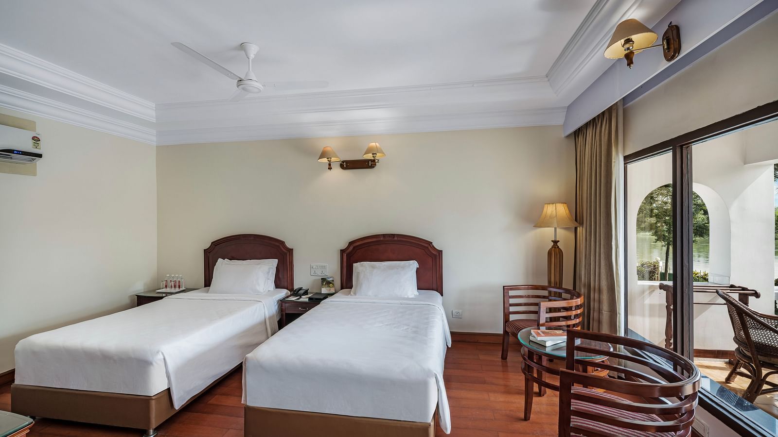 An image of the River View Room With Verandah featuring two single beds, bed side table, lamps, and chairs - GReaT Trails River View Resort Thanjavur By GRT Hotels