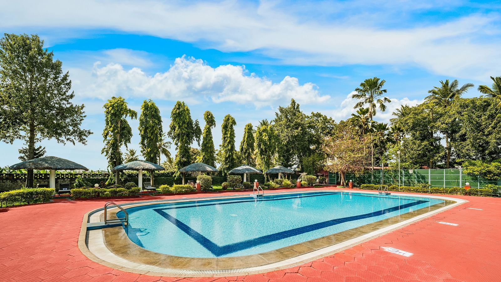 An image of a swimming pool with beautiful trees in the background - GReaT Trails River View Resort Thanjavur By GRT Hotels