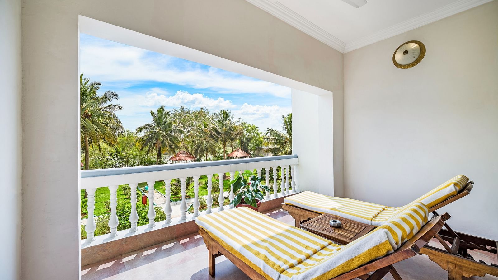 An image of a balcony of the Garden room with river view featuring two lounge chairs over viewing the lush greenery and the river - GReaT Trails River View Resort Thanjavur By GRT Hotels