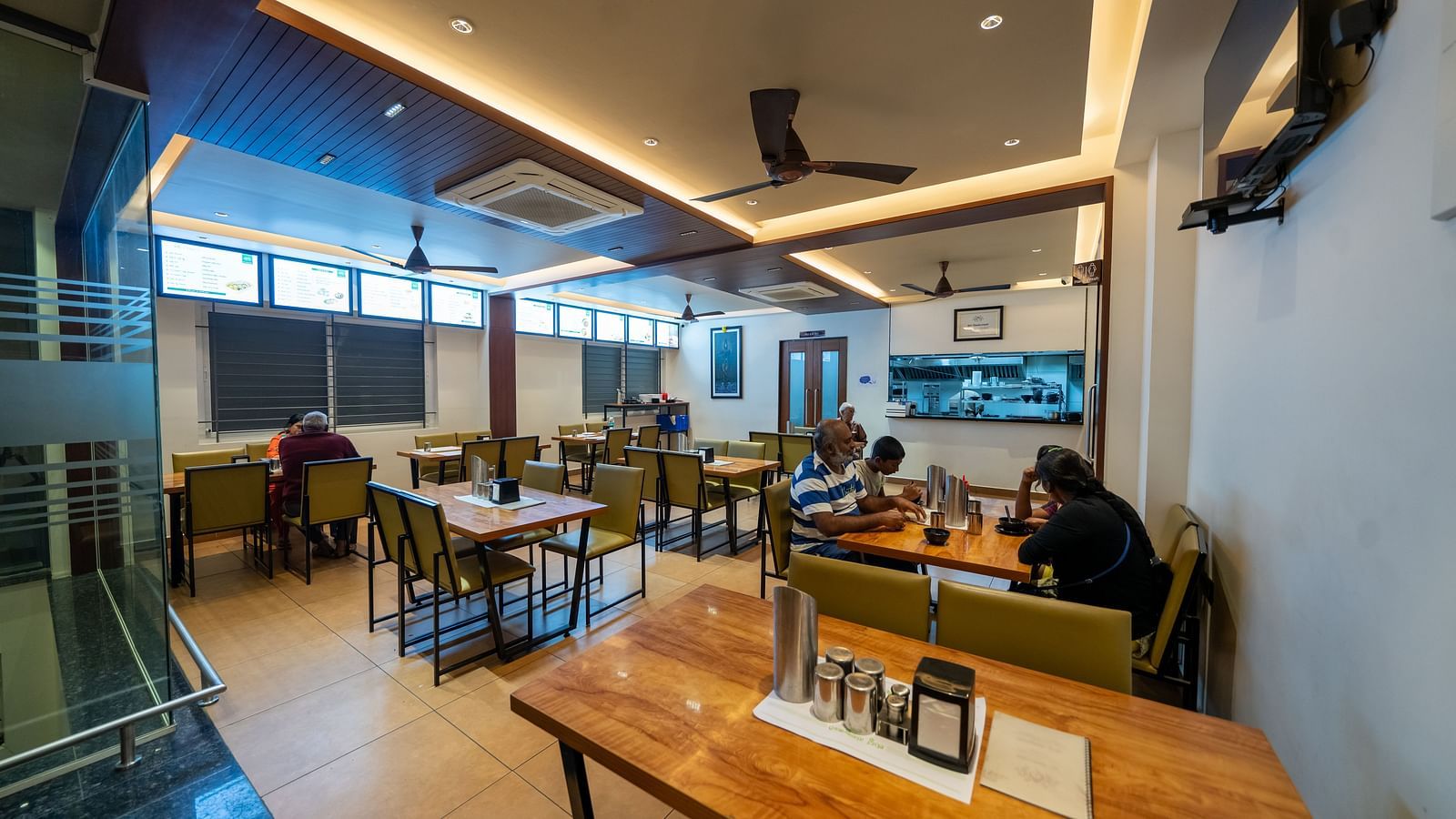 Diagonal view of the dining area at Hari Govinda's, with a neatly arranged table and chairs, and lighting featured in the ceiling corner
