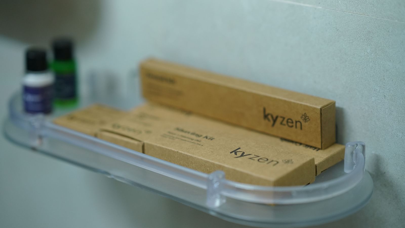 A shower shelf in a room at Kyzen Smart Stays in Hyderabad featuring hotel amenities like toothbrushes and small bottles, labelled Kyzen, indicating hospitality.
