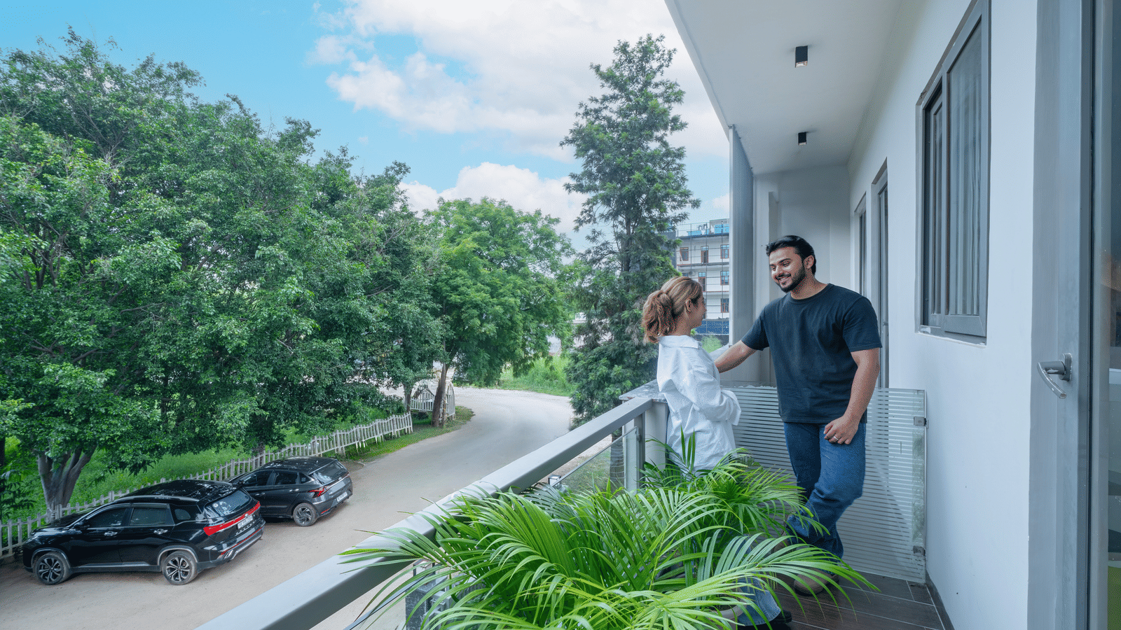 Guests walking along a balcony corridor of Lime Tree Hotels & Service Apartment Private Limited with greenery and street views.
