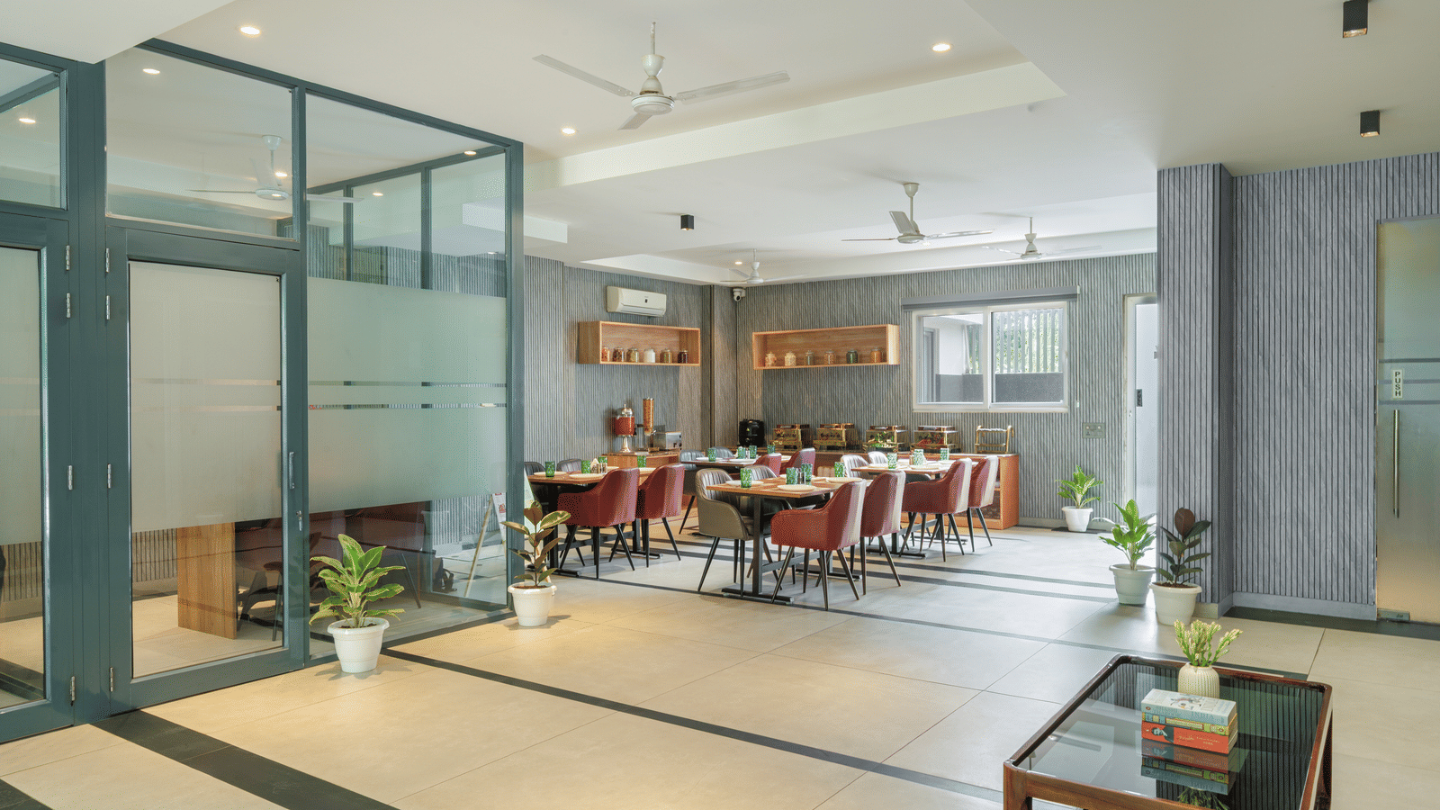 Restaurant of Lime Tree Hotels & Service Apartment Private Limited featuring glass partitions, red chairs, and dining tables.