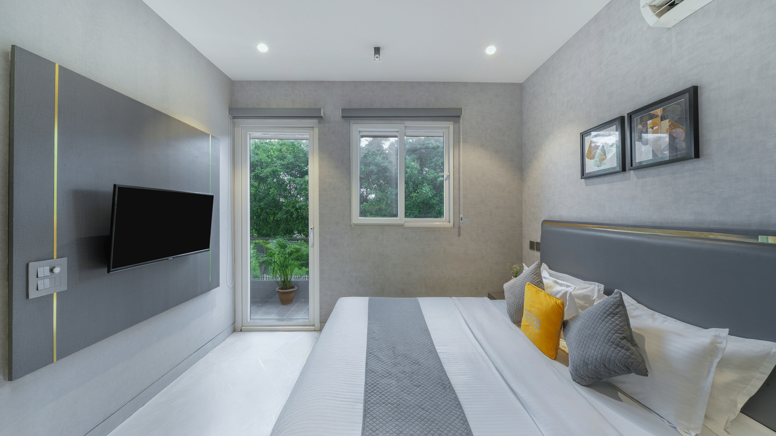 Bedroom of Lime Tree Hotels & Service Apartment Private Limited featuring a grey headboard, yellow cushions, and a wall mounted television.