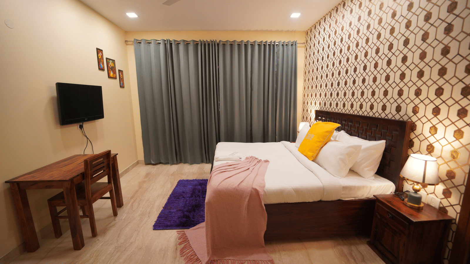 Bedroom of Lime Tree Hotels & Service Apartment Private Limited featuring a patterned headboard, a study desk, and a wall mounted television.