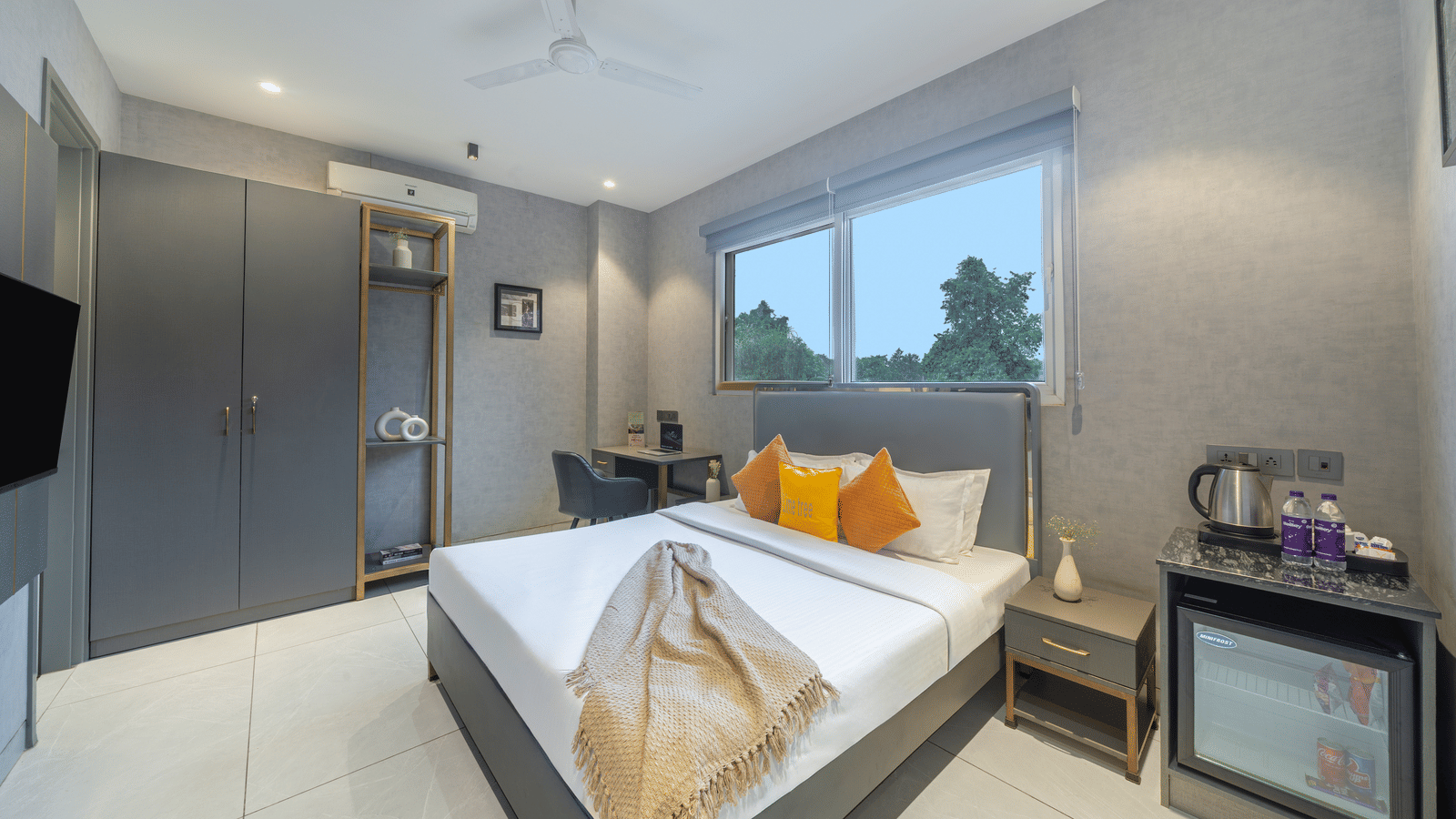 Bedroom of Lime Tree Hotels & Service Apartment Private Limited featuring a bed with yellow cushions, a television, and a large window.