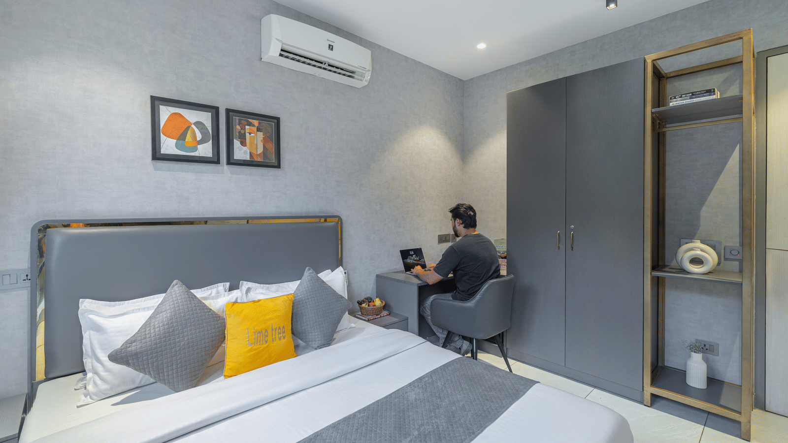 Bedroom of Lime Tree Hotels & Service Apartment Private Limited featuring a bed with yellow cushions, a work desk, and an air conditioning unit.