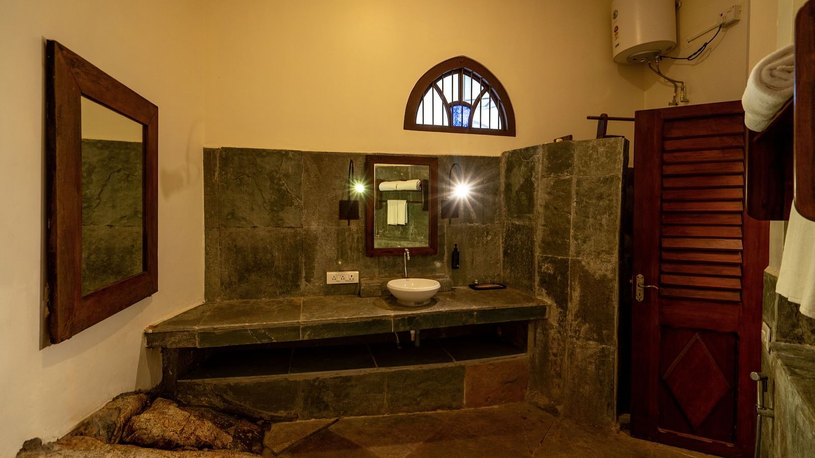 An image of a bathroom which has a mirror, a sink, geysar, cupboard, and a ventilator | Mango Hill, Yercaud