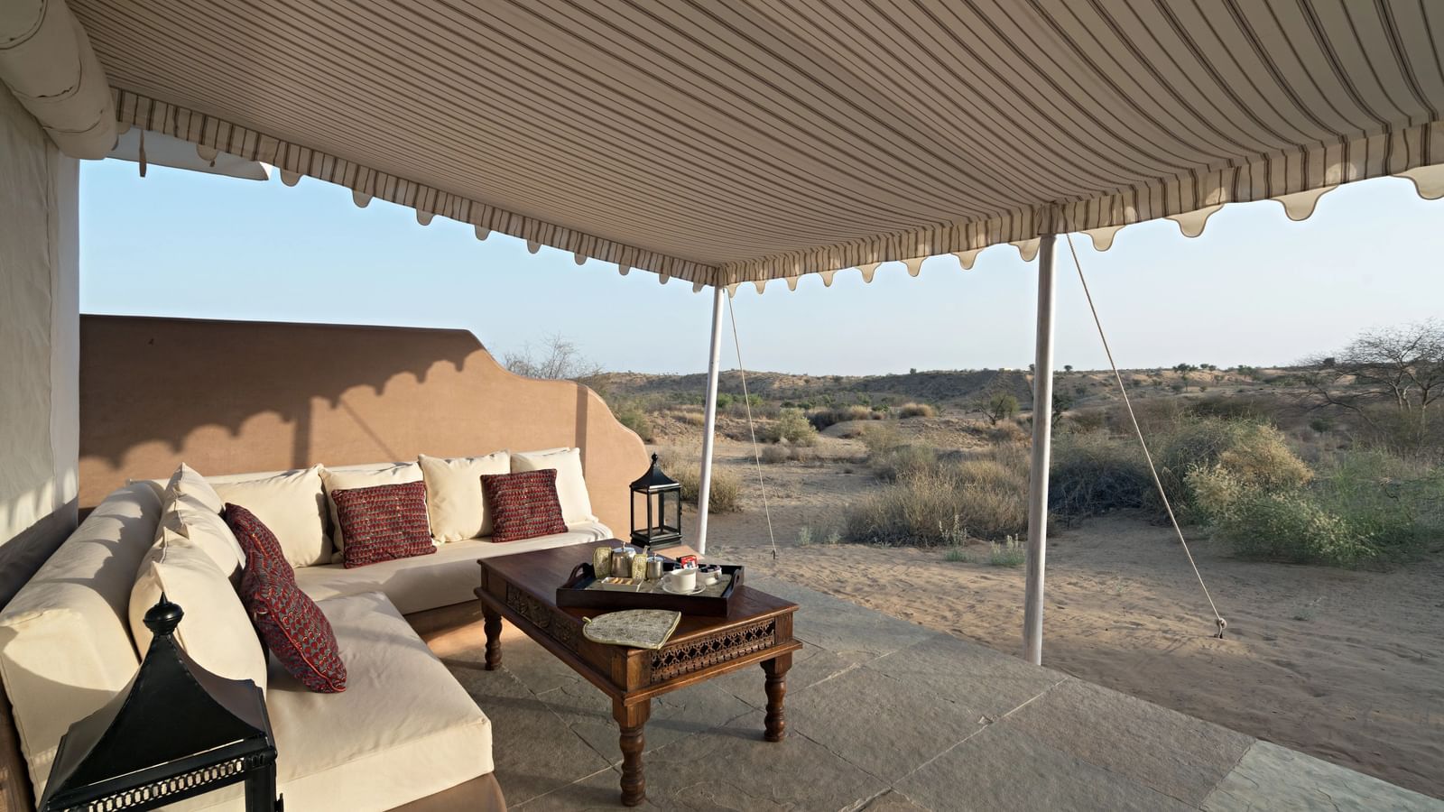 Seating area at the courtyard outside the tent of MANVAR Kumat Thar Serenity Camp featuring sofa set and centre table, and a view of the desert and trees.