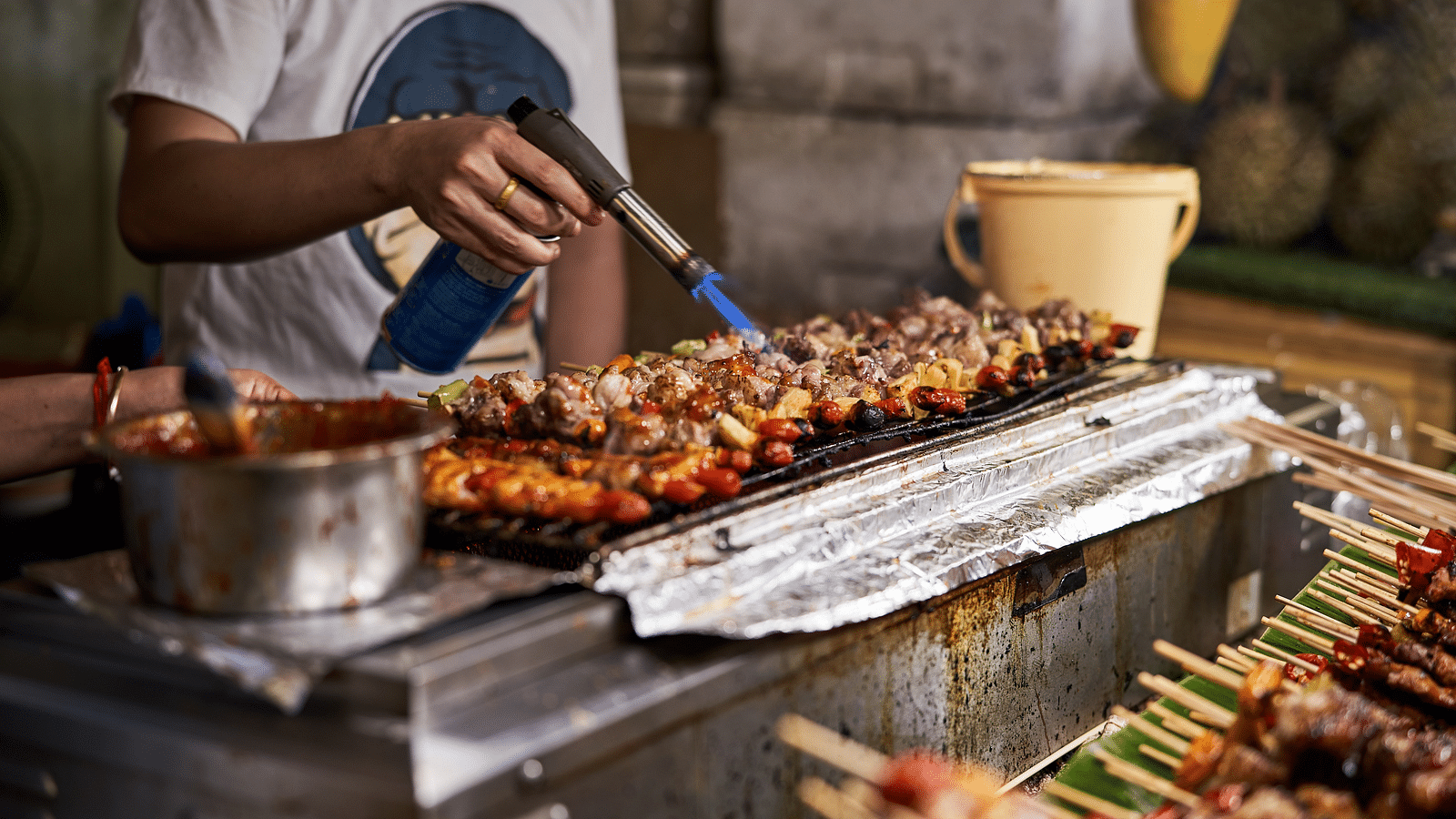 A close up shot of a street food vendor frying meat that is lined up in skewers.