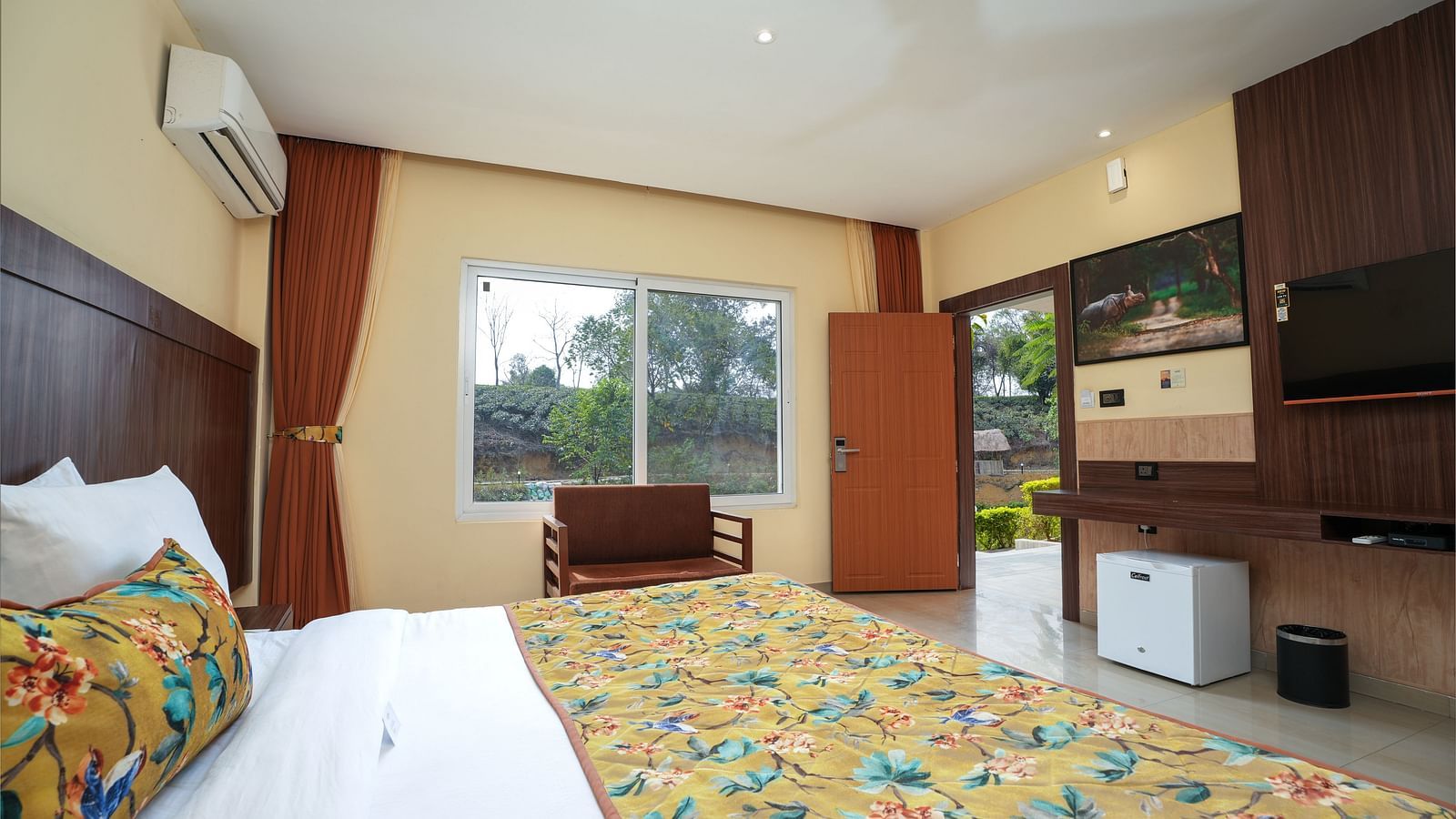 Premium Room with a large bed, wooden furniture and storage, mini fridge, air conditioning, and wall-mounted TV at Summit Green Lake Tea Resort & Spa, Kaziranga