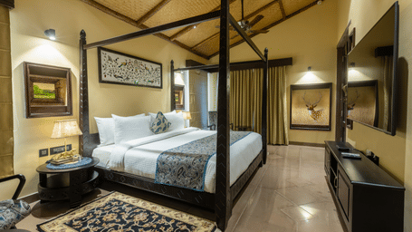 A spacious bedroom at Aamaghati Wildlife Resort with a four poster bed, elegant décor, and warm lighting creating a cosy and inviting atmosphere.