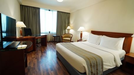 A full view of a room with a bed, TV, furniture, and a huge window at Accord Metropolitan.
