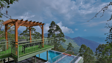 Balcony with a view of the ground-floor swimming pool, surrounded by trees and hills - Fragrant Nature Munnar