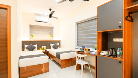 A room at Hotel Aurora Bliss, Gachibowli, featuring twin beds, spreads, pillows, a kitchenette, a sofa, a fan, a chair, and a mirror.