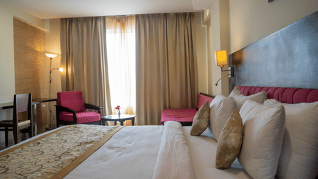 Accommodation in Udaipur featuring a large bed, armchairs, and floor-to-ceiling curtains at Hotel Udai Median, Sukhadia Circle