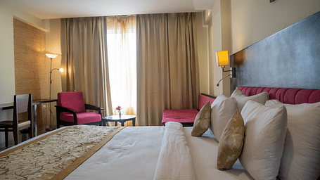 A spacious hotel room with a large bed, armchairs, and floor-to-ceiling curtains - Hotel Udai Median, Udaipur.