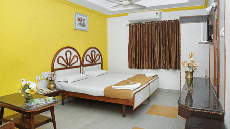 A double bedroom at Hotel Vikram with a large double bed with a wooden headboard, warm yellow interior lighting, and a seating area.