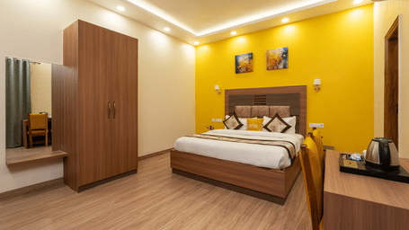 Spacious bedroom with vibrant yellow accent wall, wooden wardrobe, and modern amenities at Lime Tree Hotel & One BHK Serviced Apartment