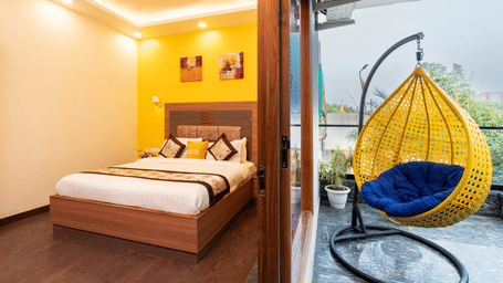 Bedroom of Lime Tree Hotels & Service Apartment Private Limited featuring a wooden headboard and a hanging egg chair by the window.
