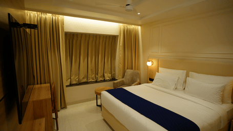  Inviting guest room at Monday Premium, Madhapur, featuring a double bed with a dark blue runner and a window with heavy gold drapes.