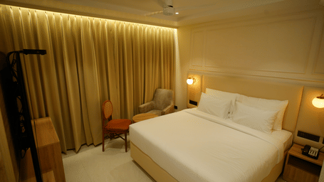 Elegant double room at Monday Premium, Madhapur, featuring a large bed, gold curtains, and a seating area with a small table.