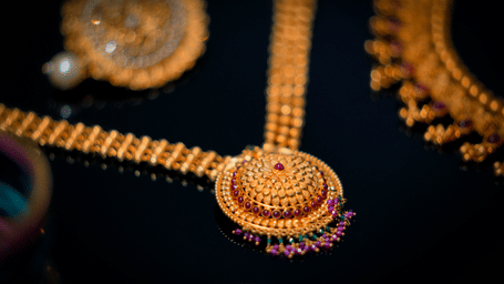 Close-up of an intricately crafted traditional South Indian gold necklace with ruby accents displayed on a black surface, highlighting fine temple jewellery craftsmanship.