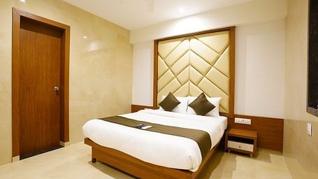 Hotel room with a double bed, patterned headboard, and closed door - Shyanu Lords Eco Inn Airoli