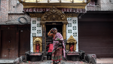 A local woman standing near an ornate, traditional stone shrine on a historic city street.