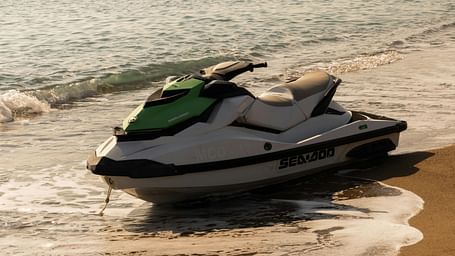 A green and white Sea-Doo jet ski moored on a sandy beach with gentle waves lapping at the shore