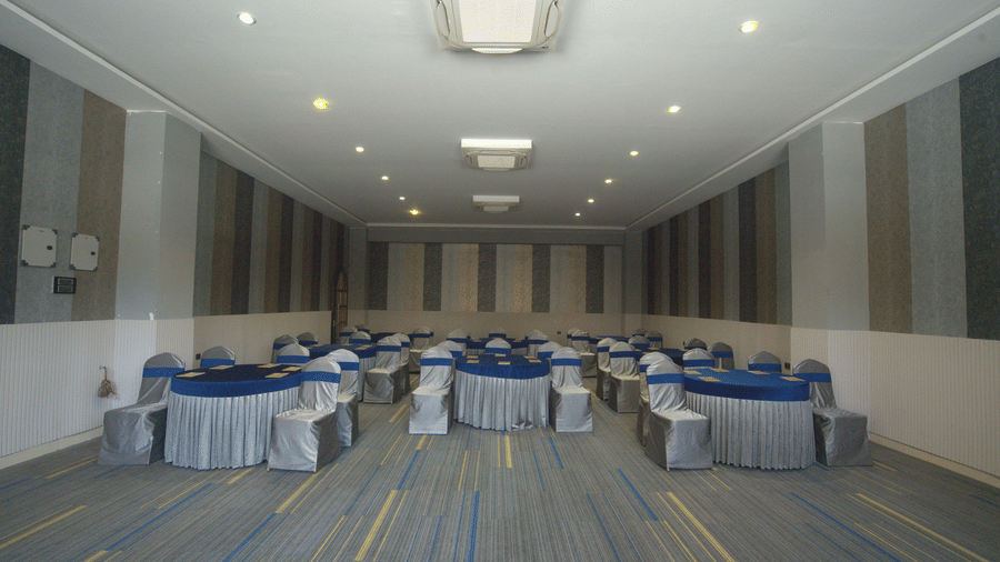 A wide shot of a spacious conference room with blue and silver table settings, patterned grey wall panels, and a blue-striped carpet at Apartel by Aarin, Oragadam.