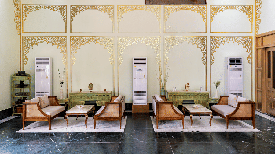 A reception area with multiple sofas, center tables, wall art, and 3 air coolers at Beelwa Palace, Jaipur.